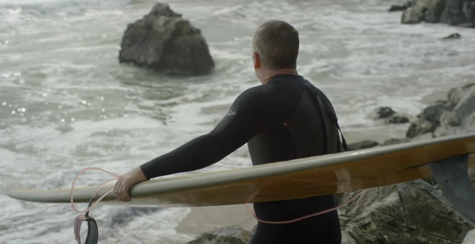 Man carrying his surfboard down some large rocks towards the beach