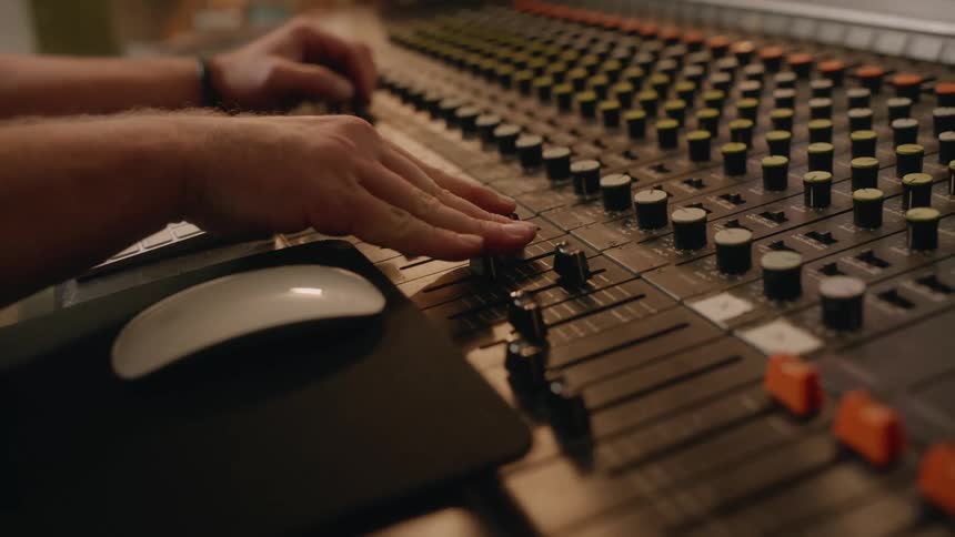 Male audio engineer working in recording studio adjust settings on audio mixing board