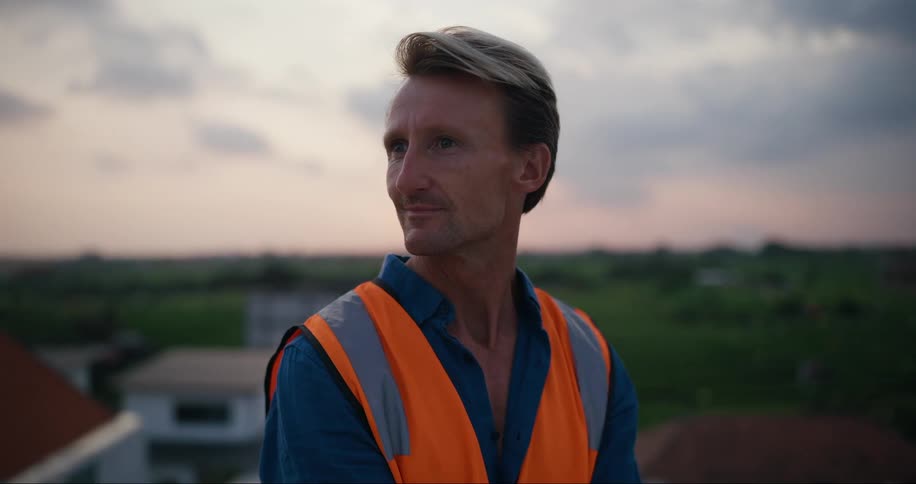 A man wearing an orange vest looks around outdoors
