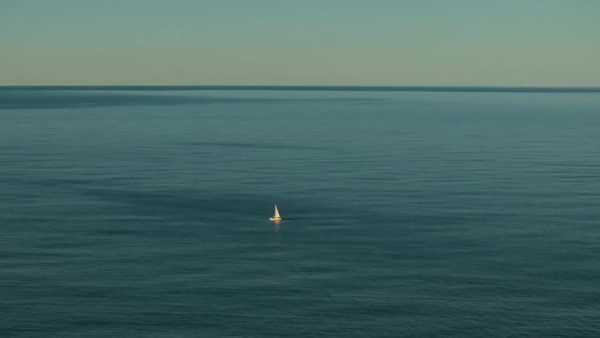 A tiny sailboat is bobbing up and down in the middle of the ocean