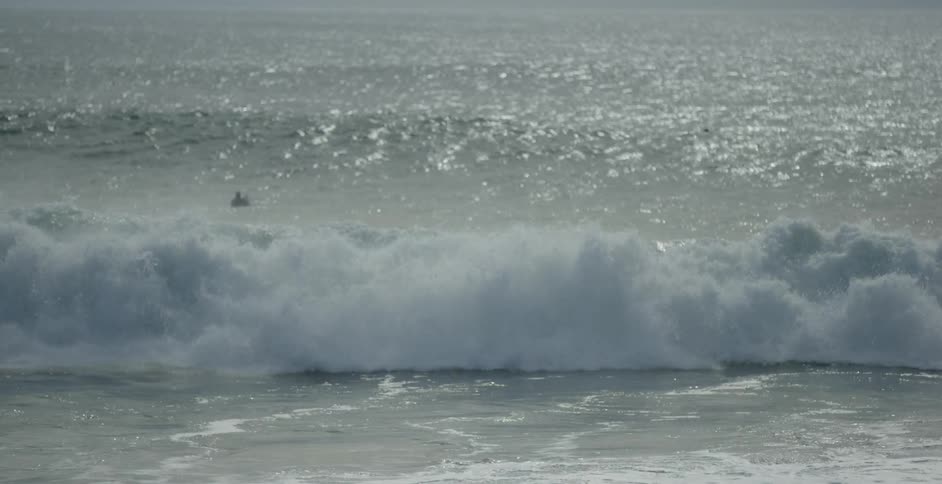 Surfers floating out in large ocean swells while waves crash onto the shore