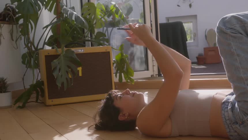 A woman uses a smartphone while lying on a wooden floor