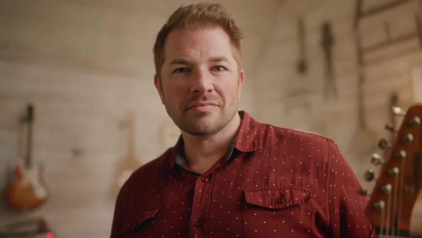 Portrait of a man giving a smile while standing in a studio and holding a guitar