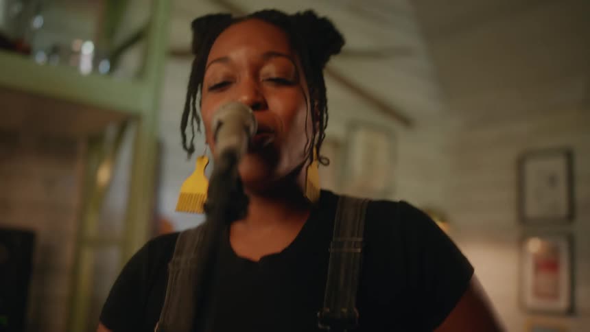 A woman sings into a microphone while moving her hands expressively