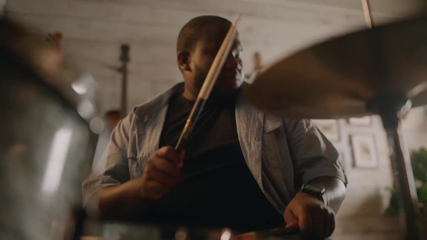 Bearded man wearing a blue shirt and a black top plays drums
