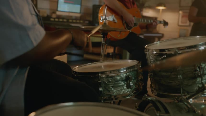 Men in a studio with one of them playing guitar and the other drums