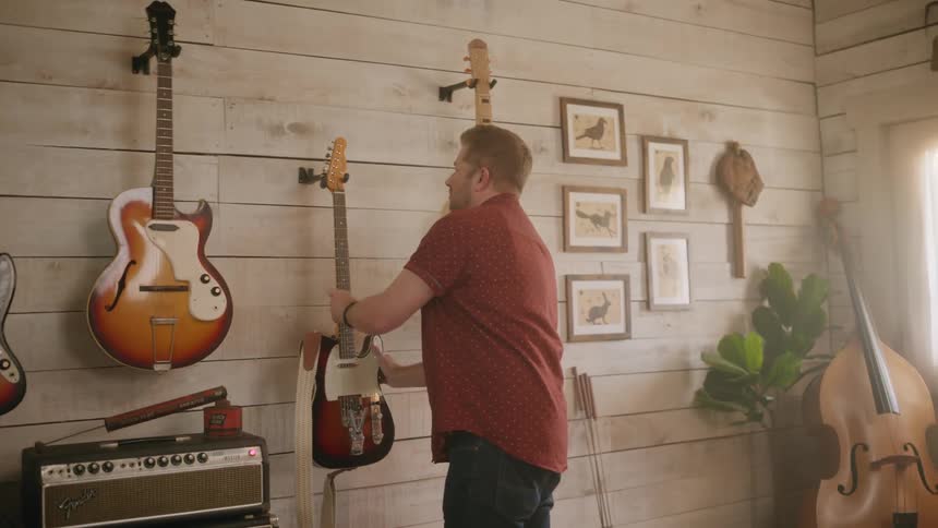 Man in a music studio placing a guitar on the wall