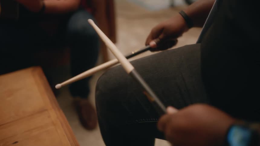 A person holding two drumsticks and hitting them on his leg