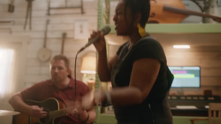 Woman singing vibrantly and next to her a man playing the guitar while they are in a studio