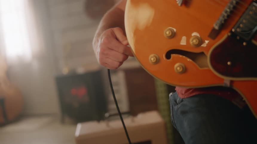 A man plugs in an electric guitar and begins playing