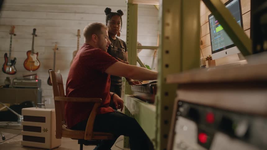 A man and a woman discuss audio tracks being edited on a sound board.