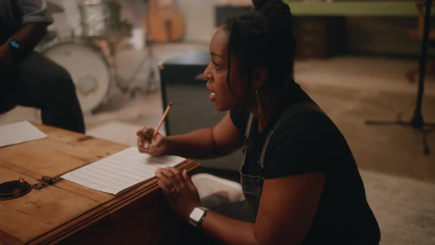 A clip of a lady in a room with friends writing music