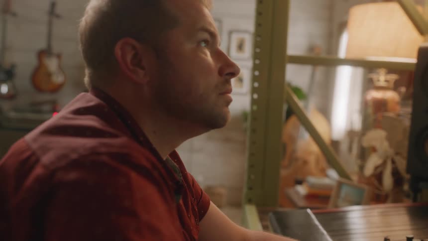 Man sitting in a chair playing with a music mixer in a studio