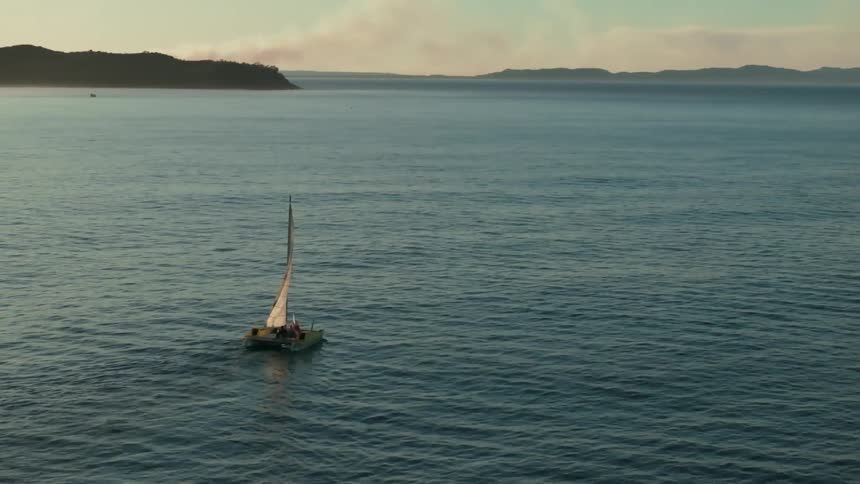 A small sailboat with white sails on a vast ocean