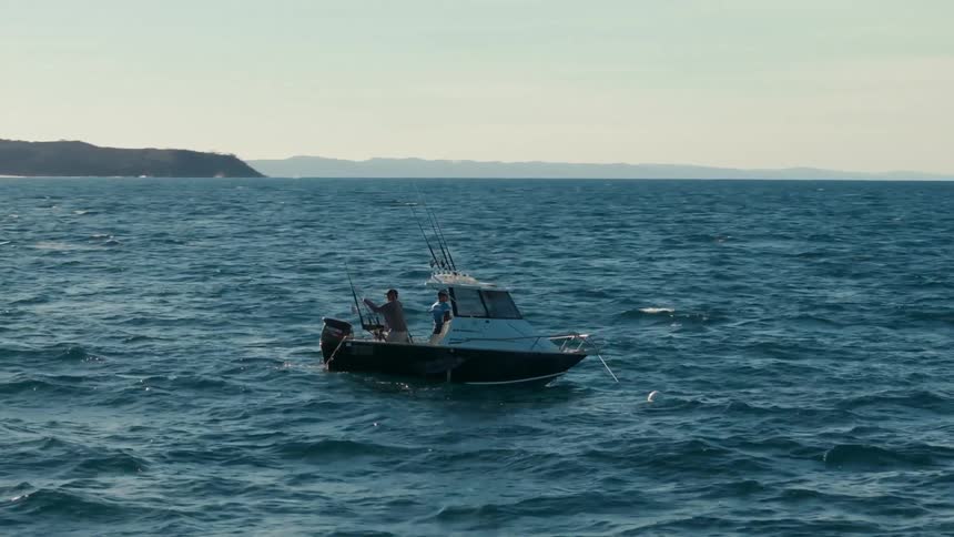 Two men fishing from a boat off of a coast