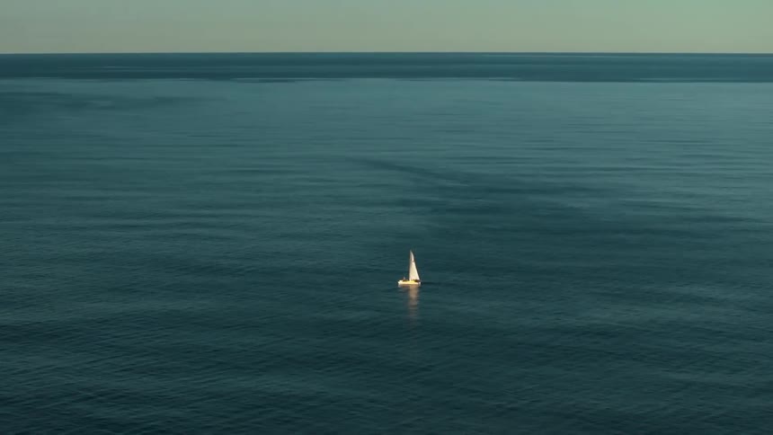 A single sailboat slowly moves across the surface of the ocean