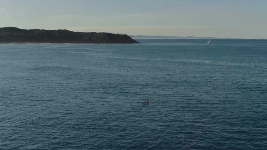 View from above of an ocean with the coast on the horizon and a moving canoe