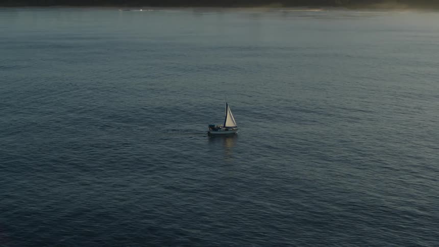 A small sailboat bobs up and down in the open sea