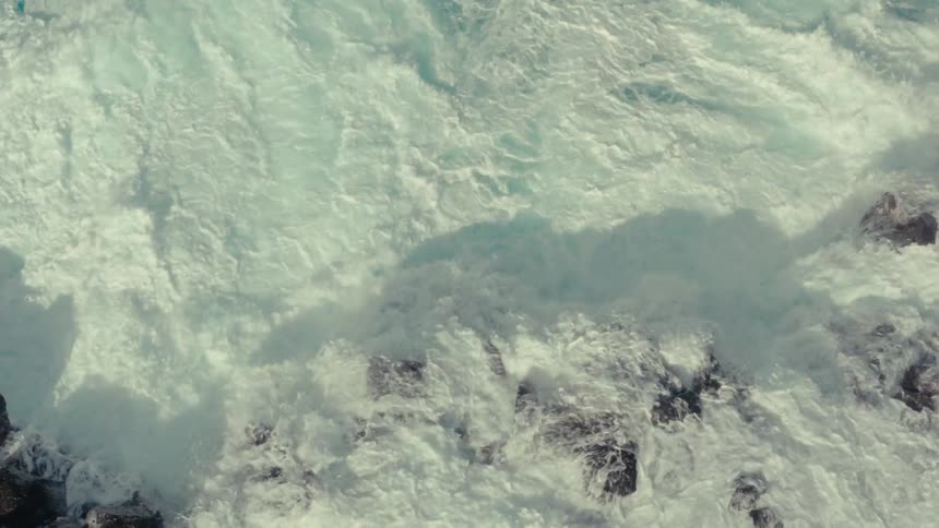 Waves foam and spray into the air while crashing against the rocky shore