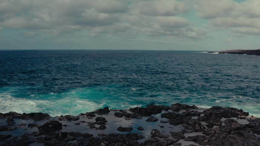 Waves crash against the rocky coast under a cloudy sky