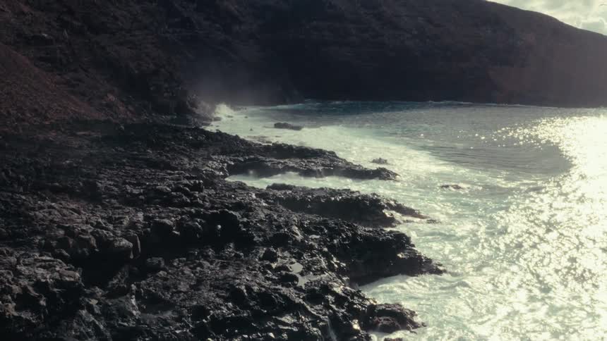 Landscape of sea waves crashing on rocky shore with sunlight reflection