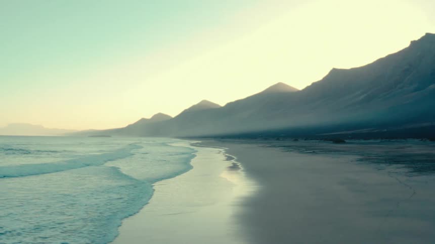 The crystalclear water laps gently at the shore of this beach with mountains in the background