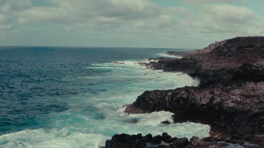 Vast blue ocean with foamy waves crashing on the rocky shore