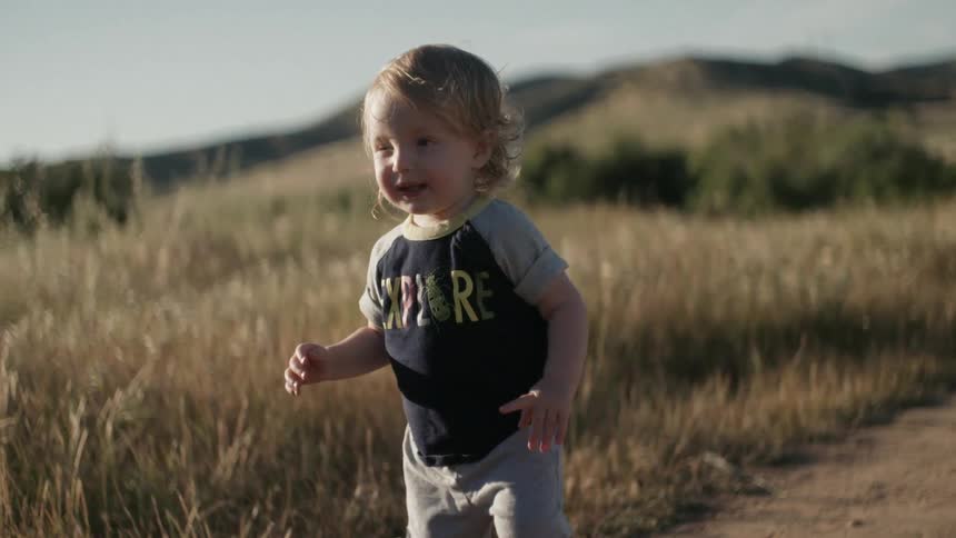 Toddler walking down a dirt road while smiling and reaching out