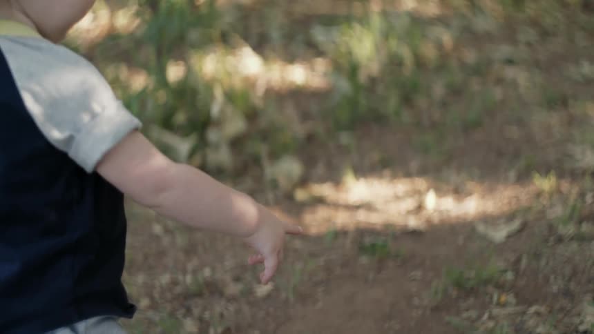 A toddler points down at something on the dirt path