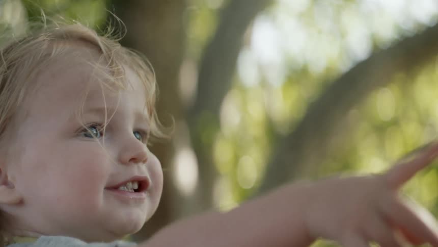 A baby points up at something and then moves her arm to the side