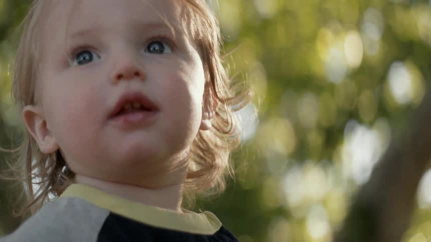 Child turning her head outside near trees during the day