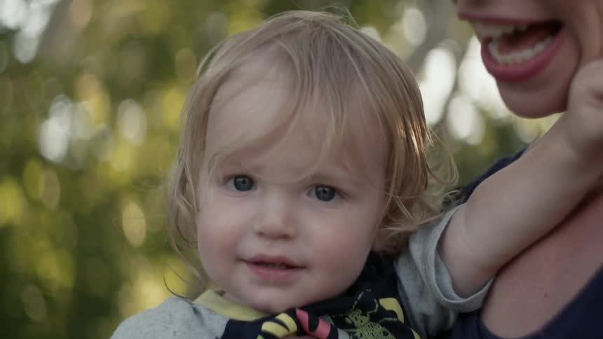 A woman is holding a toddler boy on a sunny day