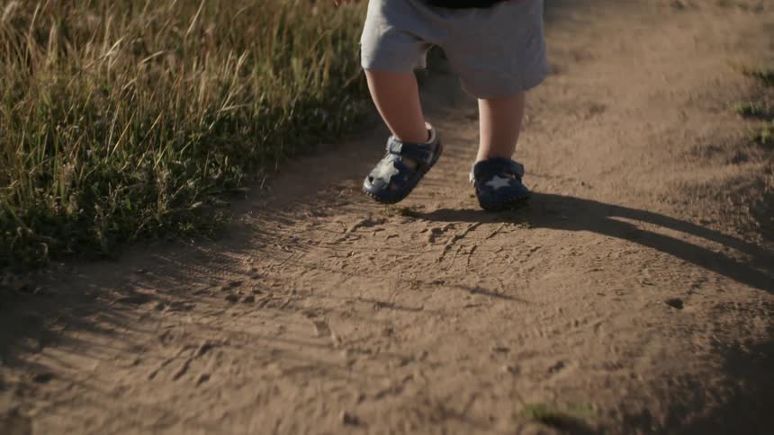 A toddler walks down a dirt path