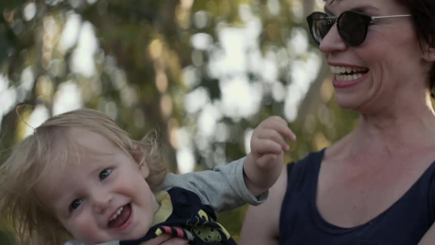 A woman swings a baby out in front of her while they both smile