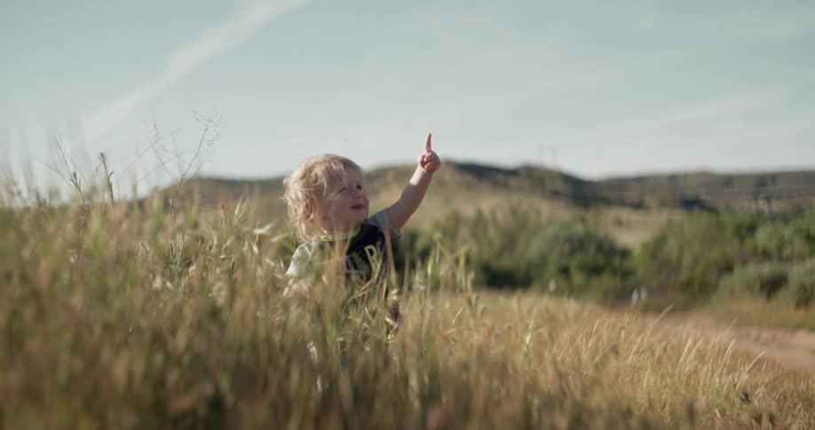A boy is pointing and laughing outdoors on a sunny day
