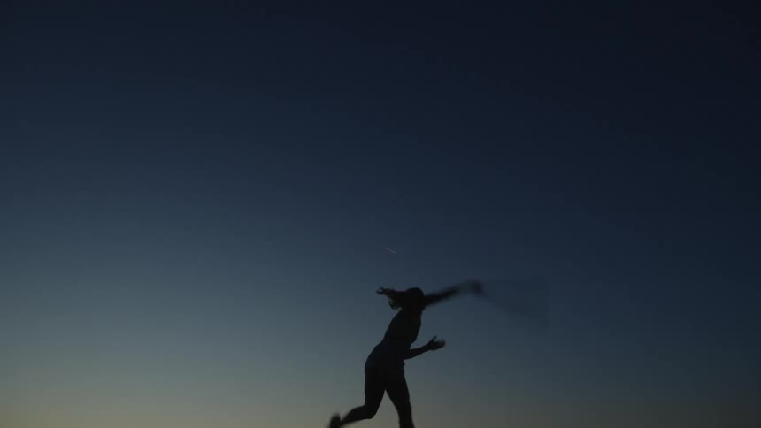 Woman silhouetted against the night sky practices her serve without a ball