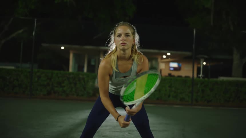Woman holding a tennis racket standing ready on the court at night