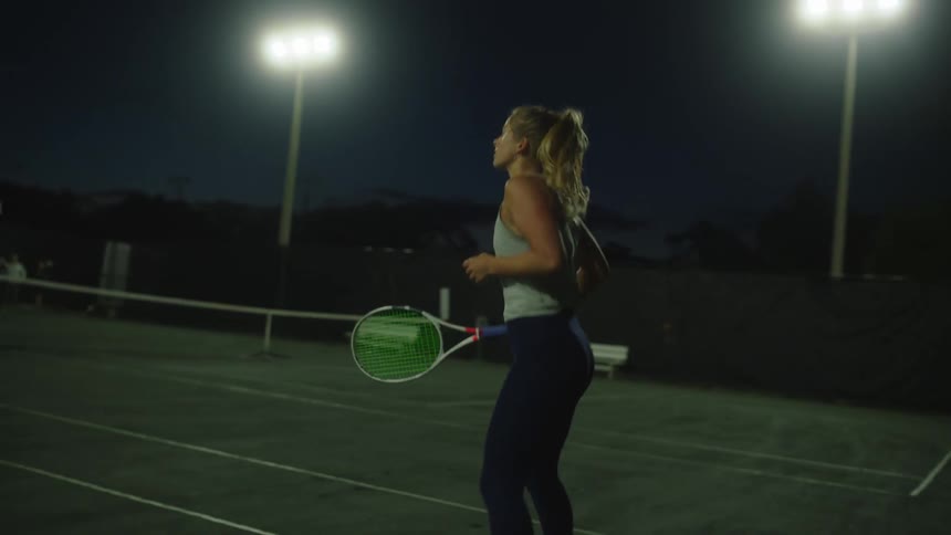 Blonde woman bouncing while playing tennis at night