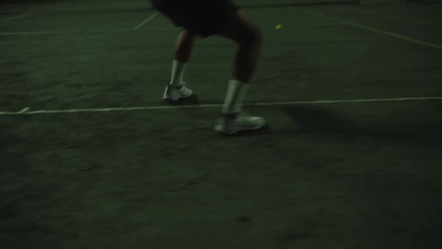 Leg of a man moving while playing on a tennis court at night