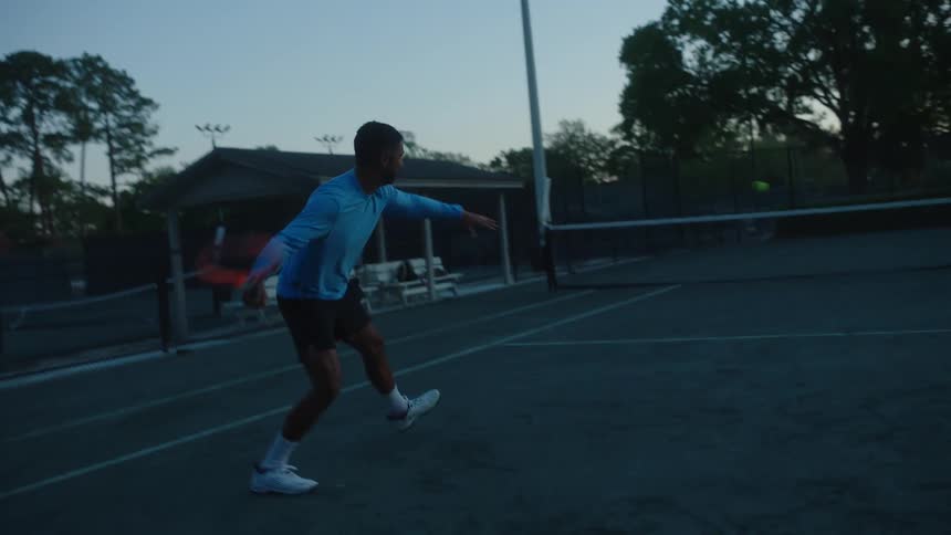 A man plays tennis on a court at dusk