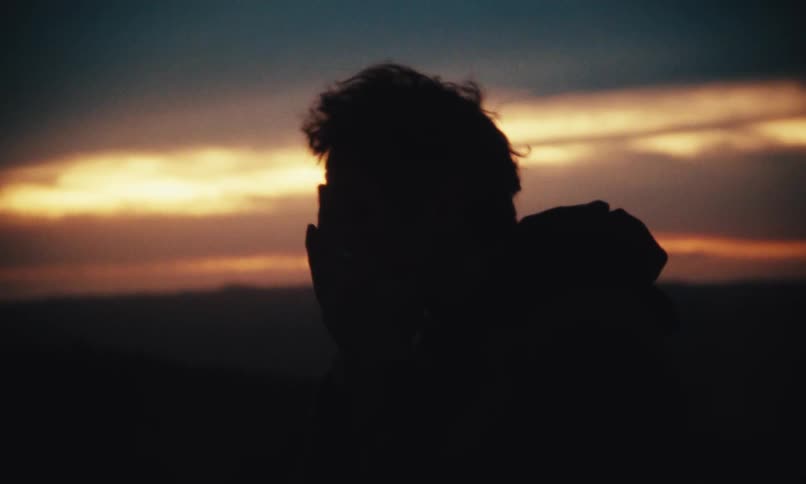 A man in silhouette wipes his face with his hands at dusk