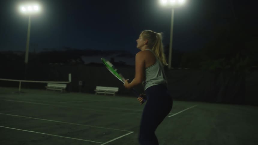 Woman hitting balls with a tennis racket on the court at night