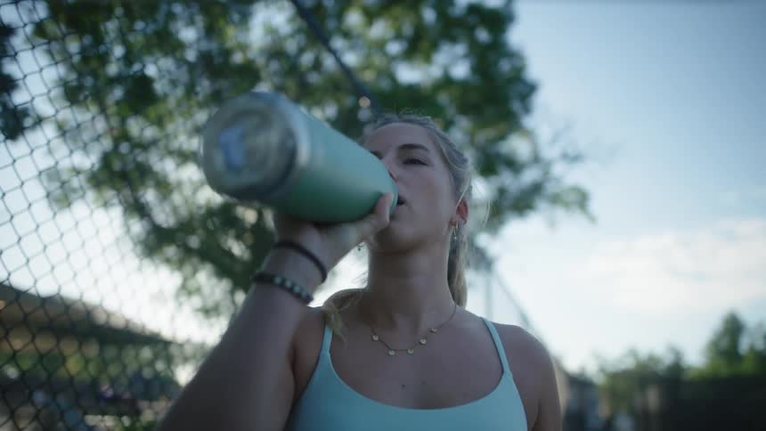 Young blonde woman drinking water from a green bottle