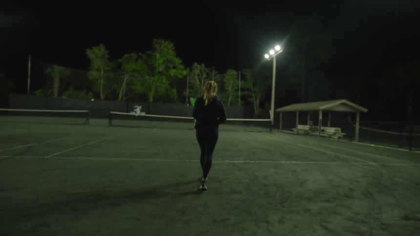 Woman holding a racket and playing tennis on a court at night