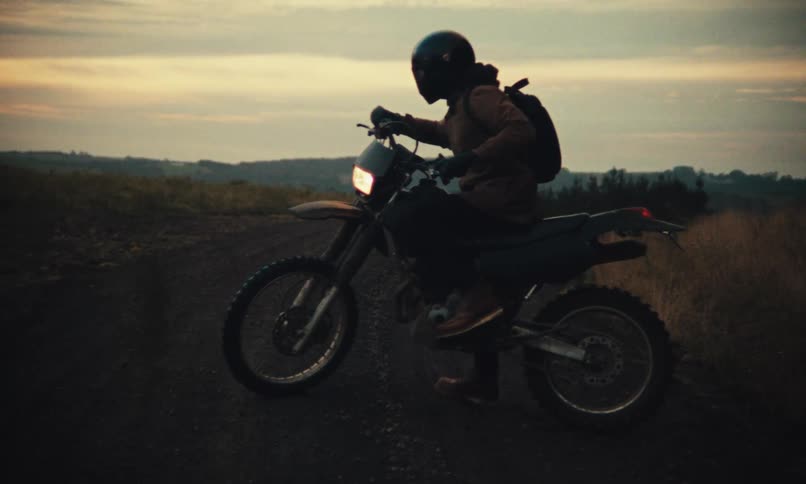 A person drives away in a motorcycle on the countryside at dusk