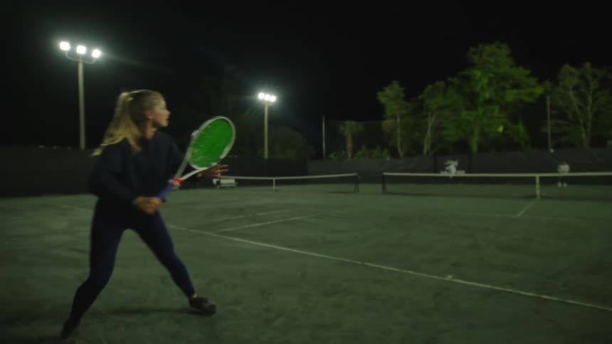 A woman is playing a game of tennis at night