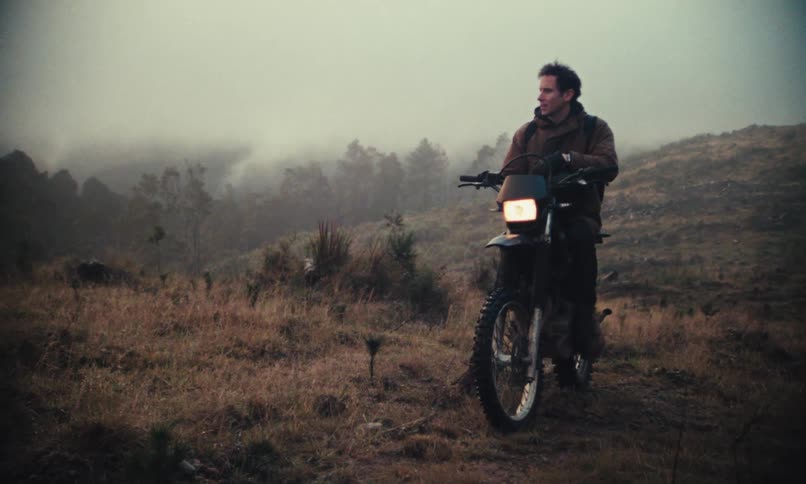 Man removing his helmet while sitting on a motorcycle on a hill in fog