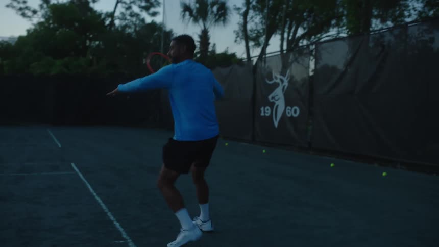A man plays tennis on an outdoor court at dusk