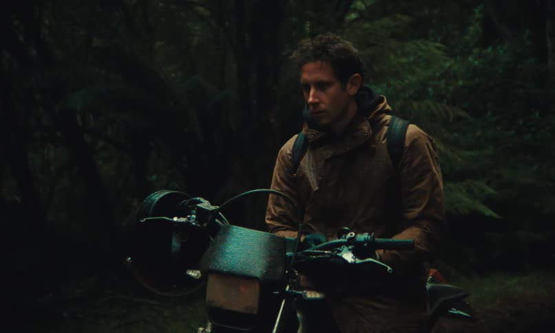 Man in the forest sitting on his motorcycle removing his helmet