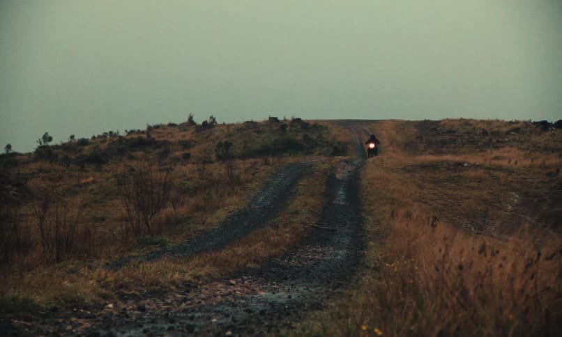 A man rides a motorcycle on a dirt path through nature